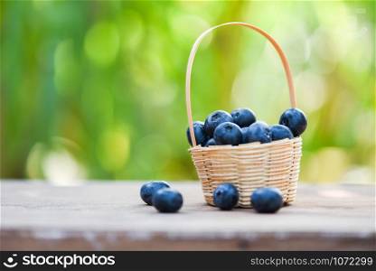 Fresh blueberries fruit in basket on wooden and nature green background - selective focus