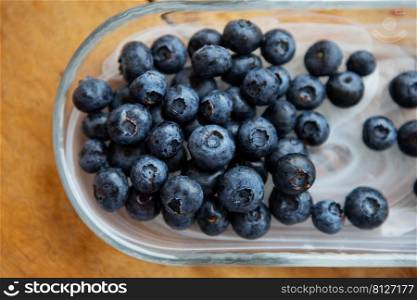 Fresh blueberries in a transparent plate on a wooden table. Top view, natural vitamins. Fresh blueberries in a transparent plate on a wooden table. Top view, natural vitamins.