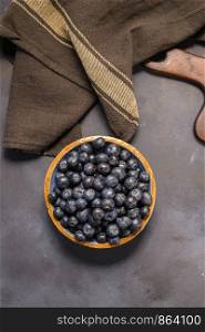 Fresh blueberries in ceramic bowl and brown cloth on dark table, rustic style.