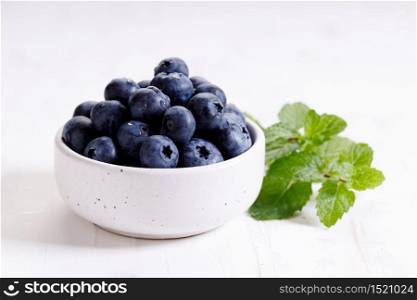 fresh blueberries in ceramics bowl with mint leaves on white wooden background.