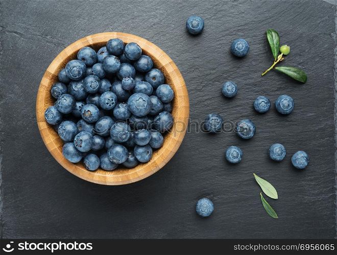 Fresh Blueberries with leaves in a bowl on dark stone background. Flat lay, top view.