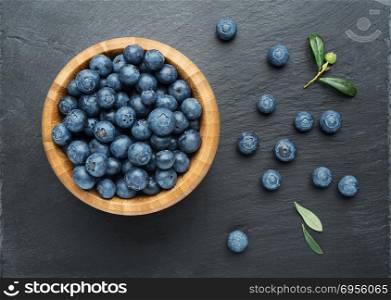 Fresh Blueberries with leaves in a bowl on dark stone background. Flat lay, top view.
