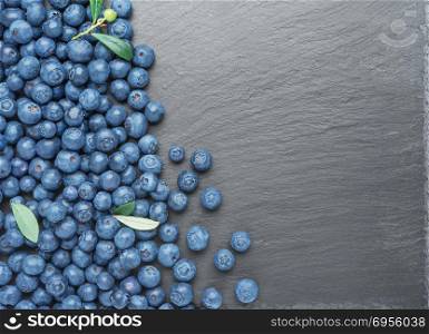 Fresh Blueberries with leaves on dark stone background. Flat lay, top view.