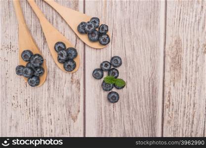 Fresh blueberries with wooden spoon and mint leaf on rustic textured background. Top of view with copy space