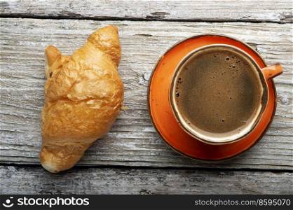 fresh boiled coffee served in beautiful orange cup with croissant around old style wooden background . close up. flat lay 