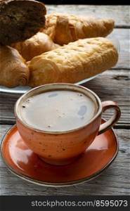 fresh boiled coffee served in beautiful orange cup with croissants around old style wooden background . close up. 