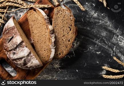 Fresh bread cut into wedges on the table, sprinkled with flour and wheat ears, top view. Healthy sourdough food and traditional rural bakery concept. Rustic style, layout on a dark table