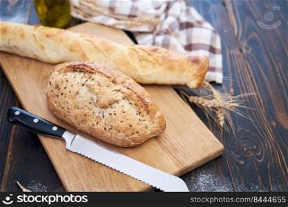 Fresh bread loaf and baguette on wooden cutting board at kitchen table.. Fresh bread loaf and baguette on wooden cutting board at kitchen table