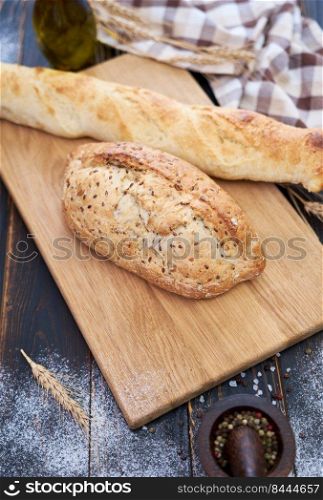 Fresh bread loaf and baguette on wooden cutting board at kitchen table.. Fresh bread loaf and baguette on wooden cutting board at kitchen table