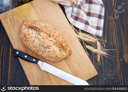 Fresh bread loaf on wooden cutting board at kitchen table.. Fresh bread loaf on wooden cutting board at kitchen table