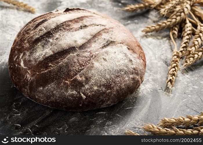 Fresh bread on a table close-up in a sprinkling of flour and wheat ears, selective focus. Healthy sourdough food and traditional bakery concept. Country style