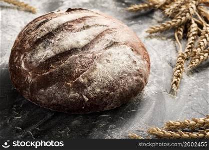 Fresh bread on a table close-up in a sprinkling of flour and wheat ears, selective focus. Healthy sourdough food and traditional bakery concept. Country style