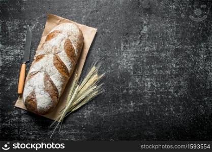 Fresh bread with spikelets and a knife. On dark rustic background. Fresh bread with spikelets and a knife.