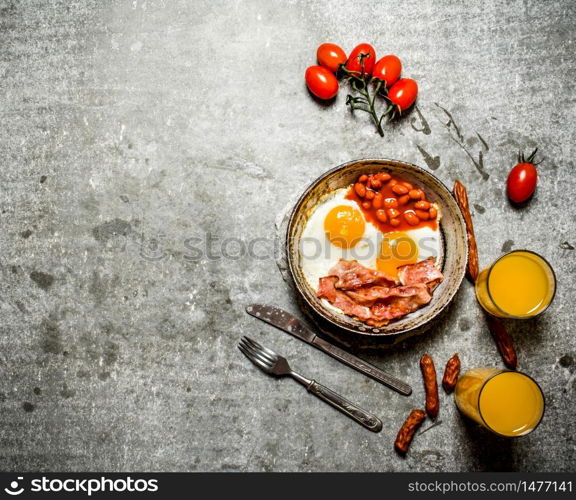 fresh Breakfast. Bacon with fried eggs and beans. Orange juice and tomatoes. On the stone table.. Bacon with fried eggs and beans.