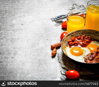 fresh Breakfast. Bacon with fried eggs and beans. Orange juice and tomatoes. On the stone table.. Bacon with fried eggs and beans.