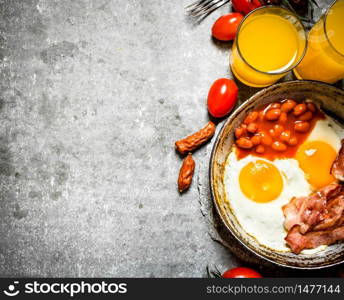 fresh Breakfast. Bacon with fried eggs and beans. Orange juice and tomatoes. On the stone table.. Bacon with fried eggs and beans.