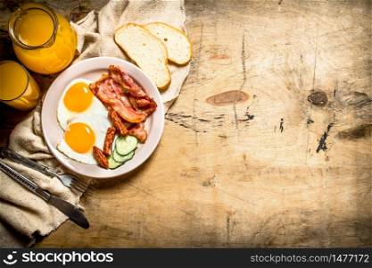 fresh Breakfast. Orange juice with fried eggs, bacon, and slices of bread. On a wooden table.. Orange juice with fried eggs, bacon, and slices of bread.