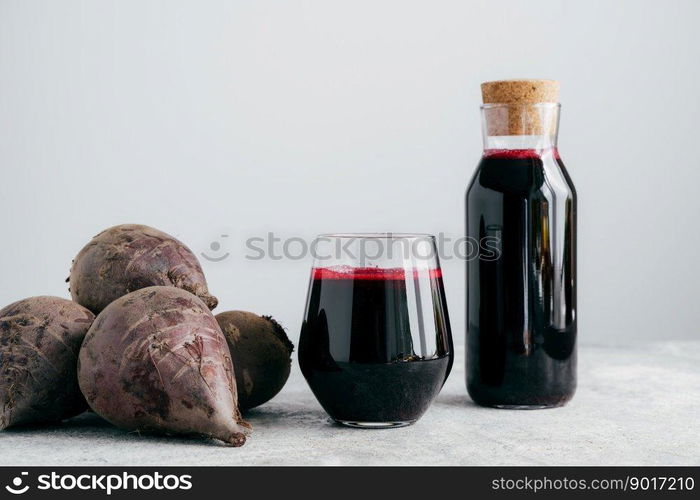 Fresh bright beetroot juice in glass bottle, raw red beet near, isolated over white background. Healthy drink. Detox natural beverage