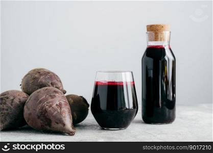 Fresh bright beetroot juice in glass bottle, raw red beet near, isolated over white background. Healthy drink. Detox natural beverage