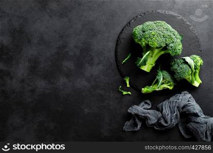 Fresh broccoli florets on black background, top view