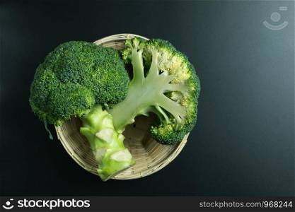 Fresh broccoli in basket on black background top view