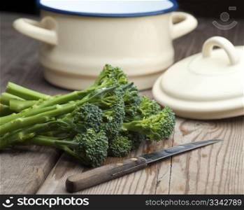 Fresh Broccoli Laid On A Wooden Kitchen Table With A Vegetable Knife and A Pan With Lid In The Background