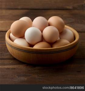 Fresh brown chicken eggs in a round wooden plate on the table