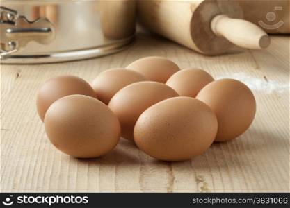 Fresh brown eggs to use for baking with a cake pan and rolling pin in the background