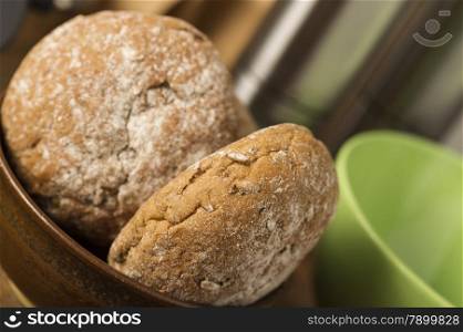 Fresh brown wholewheat rolls in a bowl. Close up high angle view of two freshly baked brown wholewheat rolls in a bowl on a kitchen counter