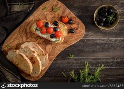 Fresh bruschetta with cream cheese, black olives and cherry tomatoes closeup.