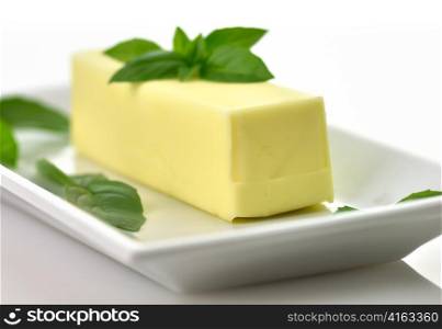 Fresh Butter stick on a white dish with basil leaves,close up