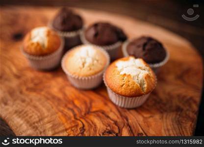 Fresh cakes with sugar and chocolate powder on wooden cutting board closeup view