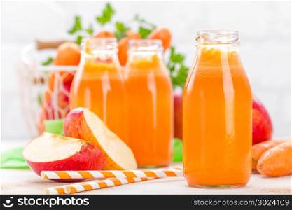 Fresh carrot and apple juice on white background. Carrot and apple juice in glass bottles on white table, closeup