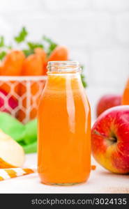 Fresh carrot and apple juice on white background. Carrot and apple juice in glass bottles on white table, closeup