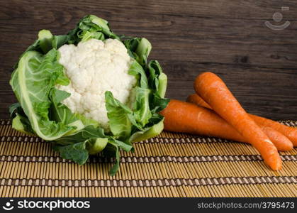 Fresh carrot and cauliflower on straw palcemat and wooden background