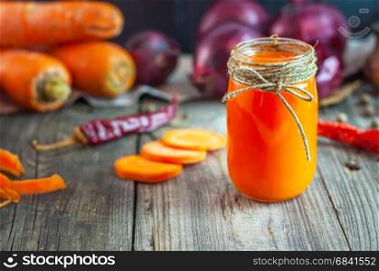 Fresh carrot juice in a glass jar among fresh carrots on a wooden table