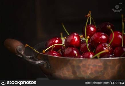 Fresh cherries in old copper pan on dark background, close up
