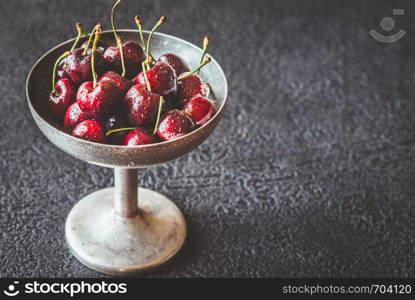 Fresh cherries in vintage silver vase on the dark wooden background
