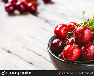 Fresh cherry berries with drops of water in a black bowl on a light vintage wooden table. Close-up with copy space.