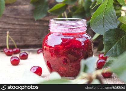 Fresh cherry jelly with fruit on a wooden background near the berries and green leaves. Close-up.. Fresh cherry jelly with fruit on a wooden background near the berries and green leaves.