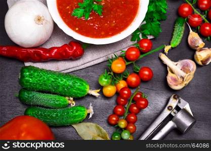 Fresh cherry tomatoes and cucumbers for cooking gazpacho soup on a black wooden background