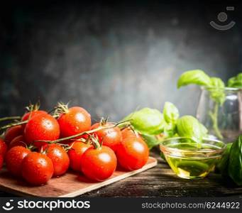 Fresh cherry tomatoes bunch with basil and oil on dark rustic background, side view, place for text. Italian food ingredients.