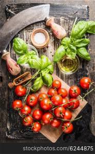Fresh cherry tomatoes bunch with basil , salt and oil on rustic wooden background, top view. Italian food cooking ingredients.