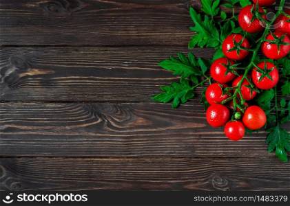 Fresh cherry tomatoes on a branch with leaves in the upper corner on a dark wooden background. Ripe tomatoes in droplets of water. Copy space for text, flat lay
