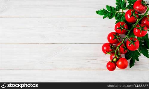 Fresh cherry tomatoes on a branch with leaves in the upper right corner on a white vintage wooden background. Ripe tomatoes in droplets of water. Copy space for text, flat lay.