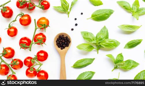 Fresh cherry tomatoes with black pepper and basil leaves on white background.
