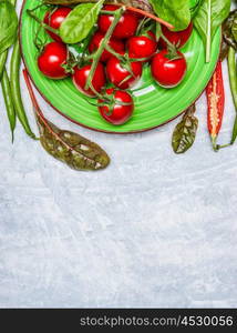 Fresh cherry tomatoes with fresh seasoning in green plate on gray wooden background, top view