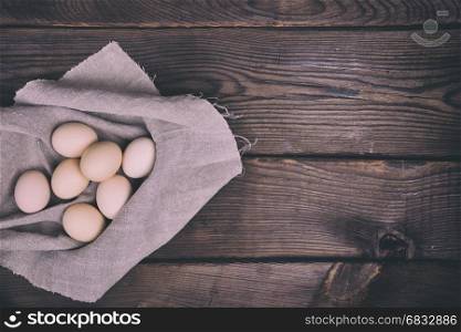 Fresh chicken eggs in shell lie on cloth gray napkin, brown wooden background with free space on the right