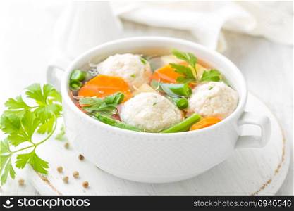 Fresh chicken soup with vegetables and meatballs in a bowl on white background. Top view