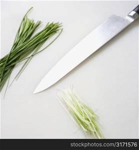 Fresh chives with kitchen knife resting on countertop.